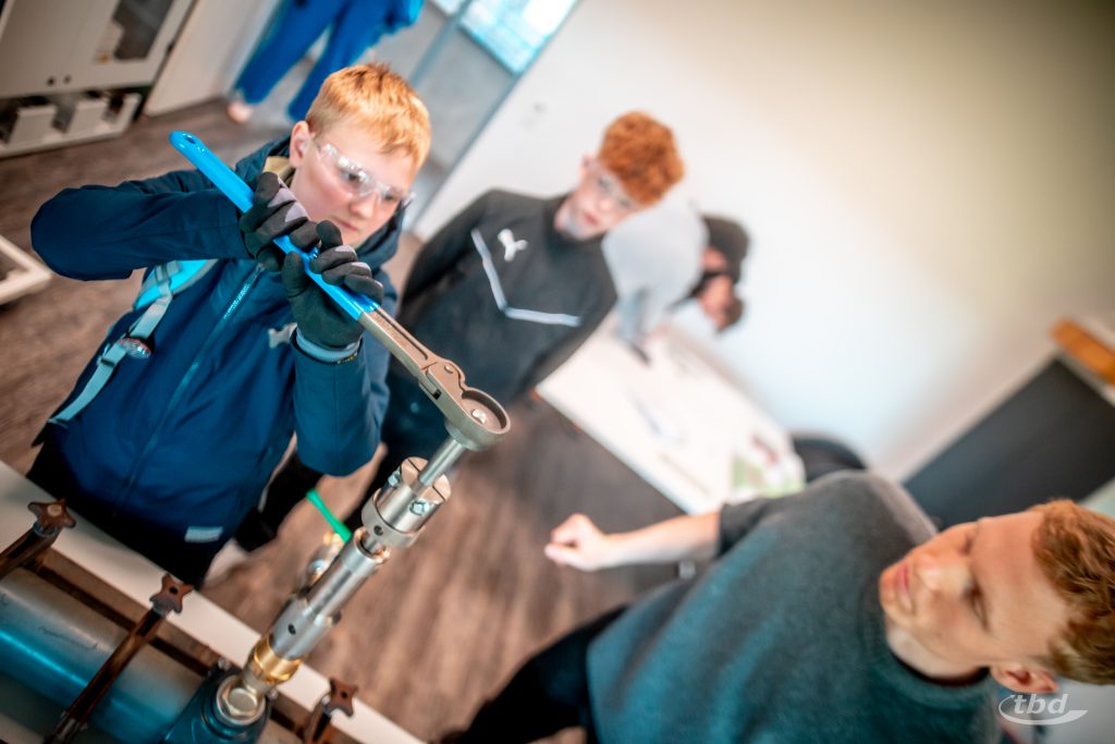 Thabo dreht die Bohrspindel, um ein Wasserrohr anzubohren. Unser Trainee Johann (rechts) und Keno (hinten) schauen zu.